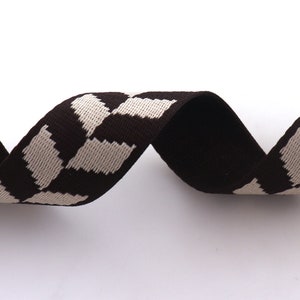 May include: Brown and white striped ribbon with a geometric pattern. The ribbon is woven and has a textured surface.