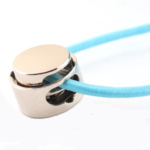 May include: A silver metal cord organizer with a blue elastic cord threaded through it.