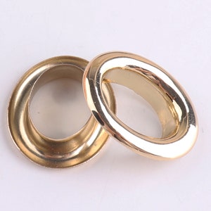 Könnte beinhalten: Zwei goldene Metallösen, eine größer als die andere, mit einer glatten, glänzenden Oberfläche. Die Ösen werden häufig für Bastelarbeiten, Kleidung und Dekoration verwendet.