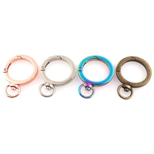 May include: Four key rings with different finishes: rose gold, silver, iridescent blue, and bronze. Each ring has a swivel clasp and a small ring.