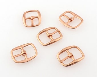 Puede incluir: Cinco cierres de hebilla de metal de color oro rosa para correas de cuero. Las hebillas son de forma cuadrada con esquinas redondeadas y tienen un acabado liso.