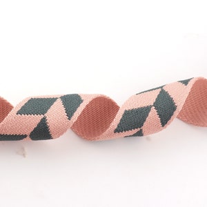 May include: A pink and dark gray woven ribbon with a geometric pattern. The ribbon is curled and twisted.
