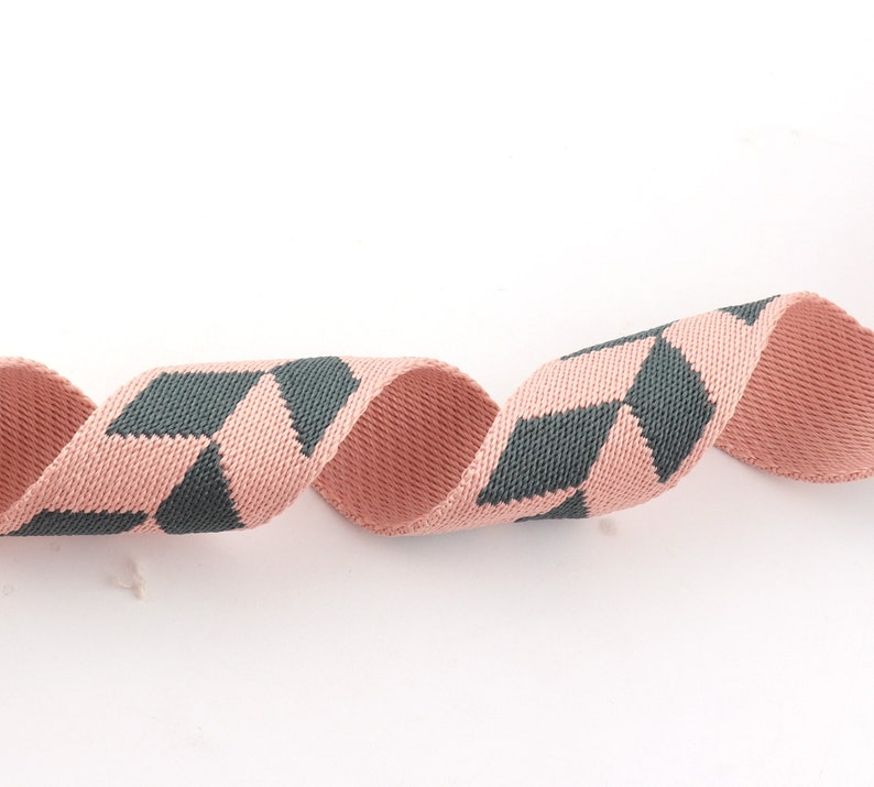 May include: A pink and dark gray woven ribbon with a geometric pattern. The ribbon is curled and twisted.