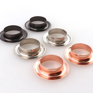 May include: Six metal eyelets in different finishes: black, silver, and copper. The eyelets are round and have a raised lip.