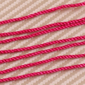 Può includere: Primo piano di un cordoncino intrecciato rosa su uno sfondo testurizzato. Il cordoncino è composto da più fili sottili intrecciati insieme per creare una texture simile a una corda.