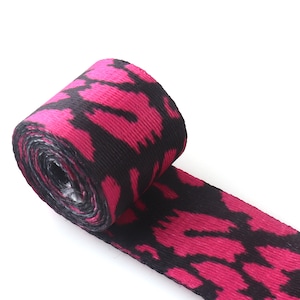 May include: Pink and black patterned webbing ribbon. The ribbon is rolled up and the pattern is visible on the surface.