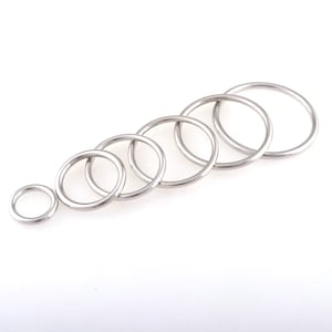 Könnte beinhalten: Ein Satz von sechs silbernen Metallringen in verschiedenen Größen. Die Ringe sind in abgestufter Größenordnung angeordnet, wobei der größte Ring oben und der kleinste Ring unten liegt.