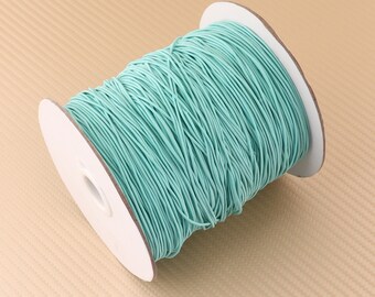 May include: A spool of light blue elastic cord. The cord is wound around a white cardboard spool.