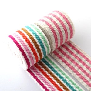 Puede incluir: Un rollo de cinta a rayas de colores. La cinta presenta rayas alternas blancas, rosas, naranjas, turquesas, verdes y marrones. La cinta está desenrollada, revelando el patrón. Adecuada para diversos proyectos de manualidades.
