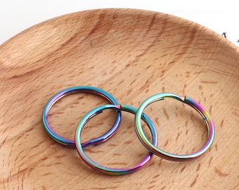 May include: Three iridescent key rings, each with a smooth, round shape, are arranged on a wooden surface. The key rings are a vibrant mix of blue, green, and purple.