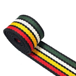 May include: A black, red, yellow, white, and green striped webbing strap. The strap is rolled up and the end is laying flat.
