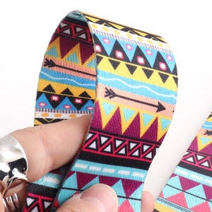 Puede incluir: Primer plano de una correa de tela con estampado colorido con un diseño geométrico que presenta triángulos, flechas y líneas onduladas en tonos de azul, amarillo, rosa, rojo y negro.