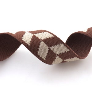 May include: Brown and white patterned woven ribbon. The ribbon has a geometric pattern with white squares on a brown background.