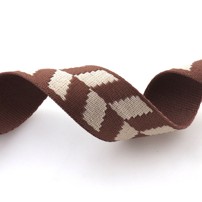 May include: Brown and white patterned woven ribbon. The ribbon has a geometric pattern with white squares on a brown background.