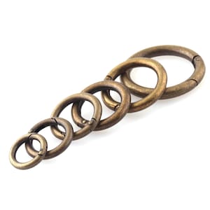May include: A set of six antique gold-toned metal key rings of varying sizes. The rings are open and have a spring-loaded closure.