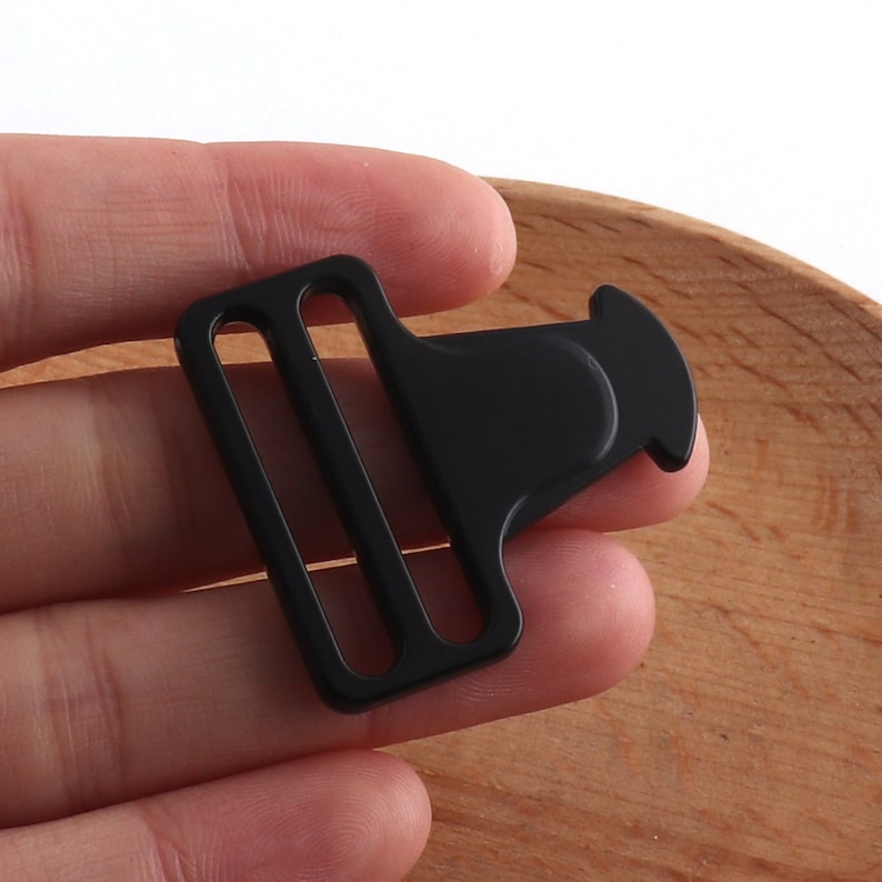 May include: Black plastic buckle with a side release clasp. The buckle has two slots for webbing.