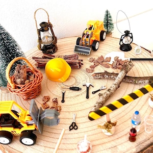 Pu&ograve; includere: Una collezione di giocattoli e accessori in miniatura a tema costruzione e campeggio disposti su una fetta di legno. Include un casco giallo, camion giocattolo, lanterne, una scopa e un cestino.