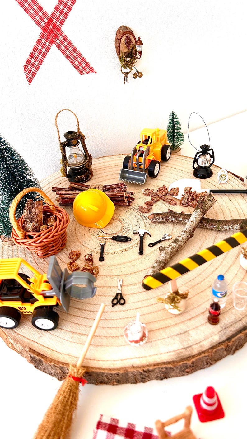 Pu&ograve; includere: Una collezione di giocattoli e accessori in miniatura a tema costruzione e campeggio disposti su una fetta di legno. Include un casco giallo, camion giocattolo, lanterne, una scopa e un cestino.