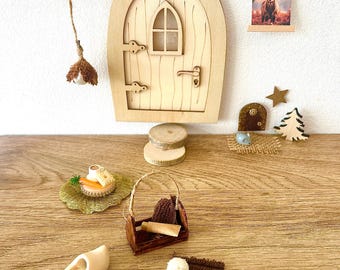 Può includere: Una porta delle fate in miniatura in legno con una piccola finestra ad arco e maniglia, accompagnata da un ornamento a ghianda appeso, un decoro da parete con cervo, un cestino con una pergamena, due zoccoli in legno, una spazzola e un piattino.