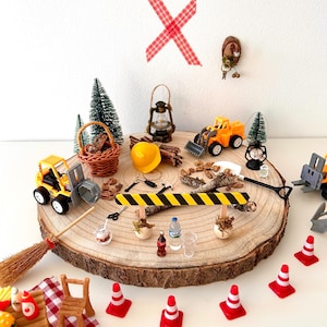 Pu&ograve; includere: Una collezione di giocattoli in miniatura a tema costruzione e picnic disposti su una fetta di legno. Include veicoli da costruzione gialli, coni stradali, un tavolo da picnic, una scopa e una lanterna in miniatura. Lo sfondo &egrave; bianco.