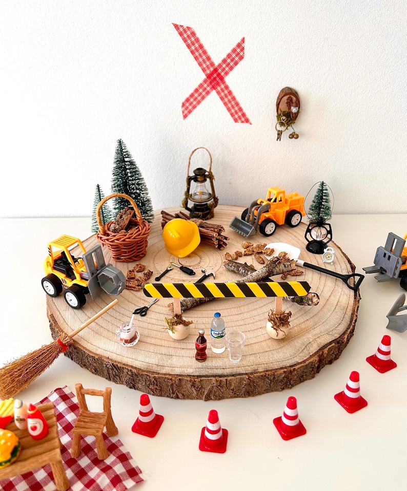 Pu&ograve; includere: Una collezione di giocattoli in miniatura a tema costruzione e picnic disposti su una fetta di legno. Include veicoli da costruzione gialli, coni stradali, un tavolo da picnic, una scopa e una lanterna in miniatura. Lo sfondo &egrave; bianco.