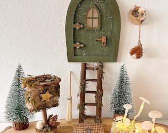 May include: A whimsical fairy garden scene featuring a green wooden door with a star, a ladder, a mailbox, a broom, a woven mat, two miniature Christmas trees, and a cluster of glowing mushroom lights. The scene is set on a wooden slice.