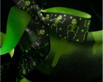 May include: Black ribbon with a repeating pattern of dancing skeletons and stars in neon green. The ribbon is tied in a bow, with bright green accents. The image has a Halloween theme.