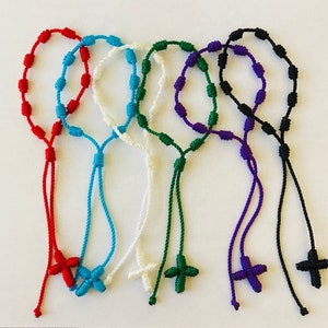 May include: Six colorful knotted rope bracelets with a cross charm at the end. The bracelets are red, blue, white, green, purple, and black.