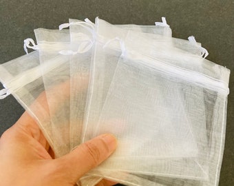 May include: A stack of white organza gift bags with a drawstring closure. The bags are made of sheer fabric and are perfect for small gifts or favors.
