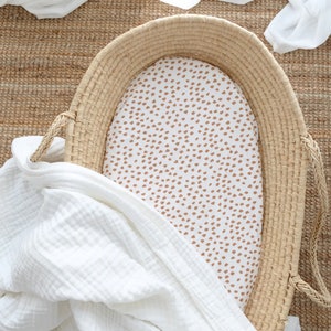 Peut inclure: Un drap-housse blanc avec un motif moucheté brun à l'intérieur d'un panier tissé. Le drap est fait d'un tissu doux et respirant, idéal pour un lit de bébé ou un berceau.