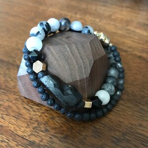 Peut inclure: Deux bracelets avec des perles de lave noire, des entretoises dorées et des perles d'agate noires et blanches. Un bracelet comprend également une pierre d'obsidienne noire.