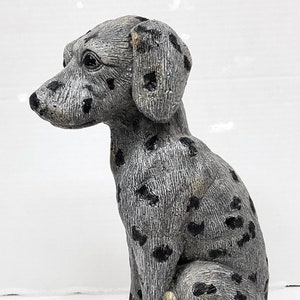 May include: A grey and black ceramic dalmatian dog figurine. The dog is sitting with its tail curled around its legs.