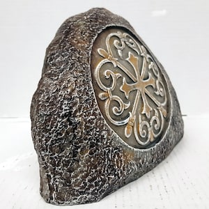 Op de afbeelding: Een decoratieve steen met een Keltisch knoopontwerp in zilver en goud. De steen is bruin en heeft een ruwe textuur.