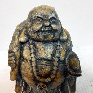 May include: A gray stone statue of a smiling Buddha with a beaded necklace. The statue is weathered and has a gold-like finish.