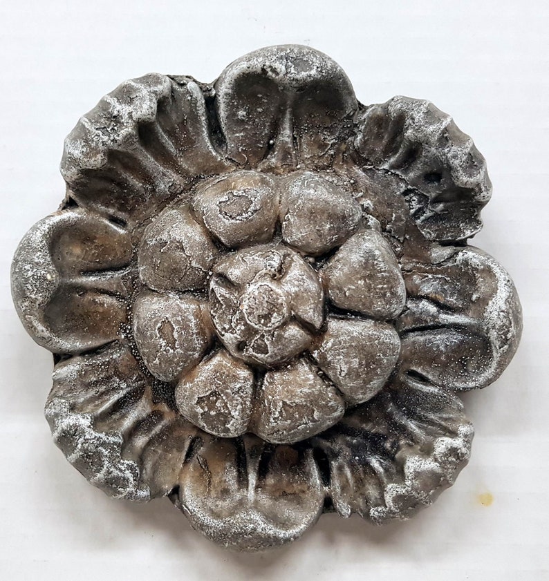 May include: A detailed, silver-toned metal floral embellishment. The decorative piece features a layered flower design with textured petals and a frosted appearance, suitable for crafts or decor.