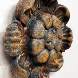 May include: A detailed, three-dimensional decorative floral element with a weathered, aged appearance. The sculpture features a complex arrangement of petals and leaves, with a color palette of bronze, brown, and black.
