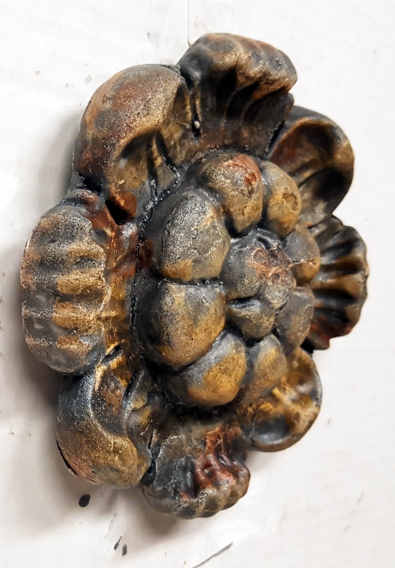 May include: A detailed, three-dimensional decorative floral element with a weathered, aged appearance. The sculpture features a complex arrangement of petals and leaves, with a color palette of bronze, brown, and black.