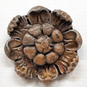 May include: A detailed, bronze-colored floral decorative element. The piece features a layered design with multiple petals and a textured surface. The color is a mix of brown and bronze with hints of silver, creating a vintage aesthetic.