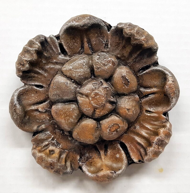 May include: A detailed, bronze-colored floral decorative element. The piece features a layered design with multiple petals and a textured surface. The color is a mix of brown and bronze with hints of silver, creating a vintage aesthetic.