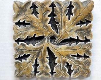 May include: A square, decorative wall plaque made of wood with a carved design of swirling leaves. The leaves are painted in shades of brown and gold.