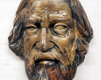 Puede incluir: Una escultura de arcilla detallada y texturizada, de color marrón y negro, que representa la cara de un hombre con barba.