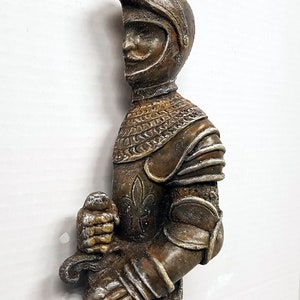 Puede incluir: Una figurita de caballero de color bronce, con armadura completa, sosteniendo una espada. El caballero lleva un casco con visera y tiene un dise&ntilde;o detallado en su armadura.