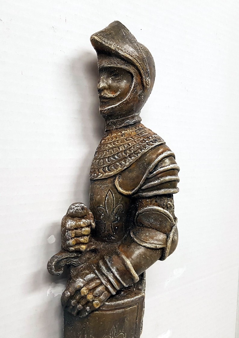 Puede incluir: Una figurita de caballero de color bronce, con armadura completa, sosteniendo una espada. El caballero lleva un casco con visera y tiene un dise&ntilde;o detallado en su armadura.