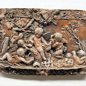 May include: A vintage-style plaster relief sculpture depicting five cherubs in a garden setting. The cherubs are sculpted in a playful and whimsical style, with one cherub holding a pitcher and another playing a musical instrument. The sculpture is painted in muted tones of brown and white, giving it a rustic and antique look.
