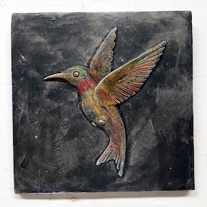 May include: A colorful hummingbird sculpture on a dark gray background. The hummingbird is made of a textured material and has a realistic appearance.