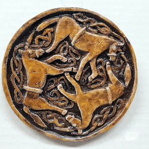 May include: A circular, brown and black, ceramic wall plaque with a Celtic knot design featuring three stylized dogs in a circular pattern.