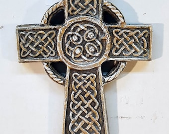 May include: A gold and brown Celtic cross with intricate knotwork designs. The cross is made of a textured material and has a raised center circle with four smaller circles inside.
