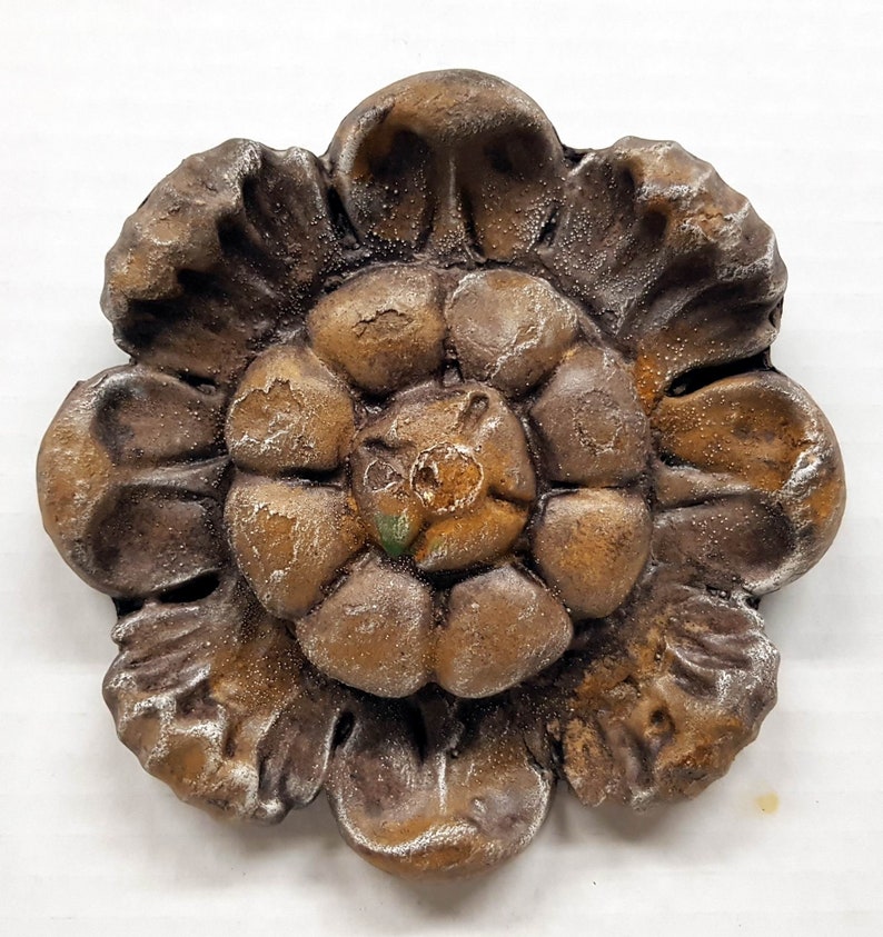 May include: A detailed, antique-style, brown and gold flower-shaped decorative element. The piece has a textured surface with visible details and a weathered appearance. The flower has multiple layers of petals and a central core.