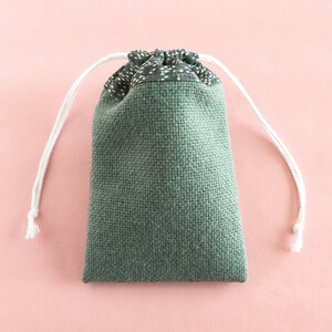 May include: A green drawstring bag with white drawstrings. The bag is made of a textured fabric and has a black and white patterned lining.