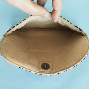 Puede incluir: Bolso de mano abierto con interior beige y exterior con estampado negro y beige. El bolso de mano se mantiene abierto, revelando el forro interior y un cierre magn&eacute;tico a presi&oacute;n. El fondo es azul claro.